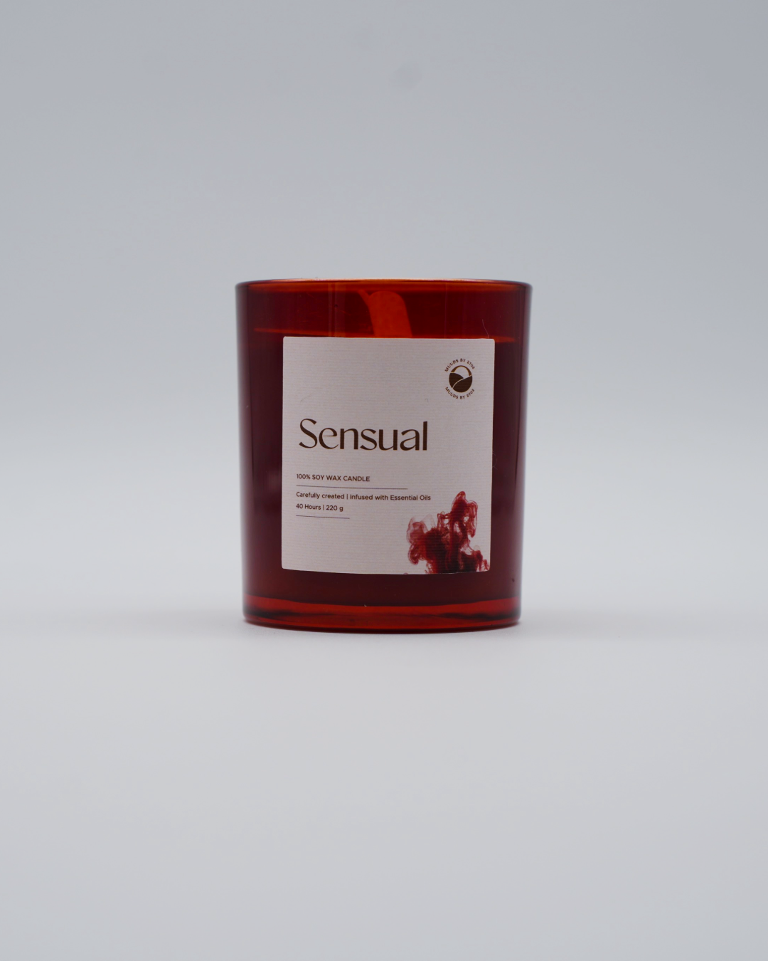 Candle with a red glass container and 'Sensual' label on a light gray background